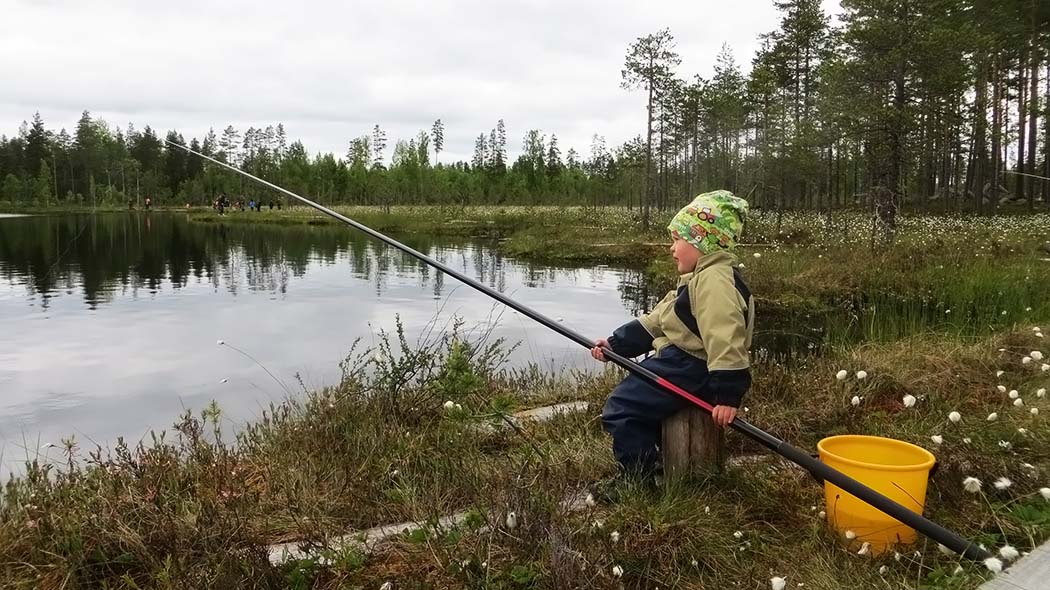 A child sits with a fishing rod by the edge of the pond.