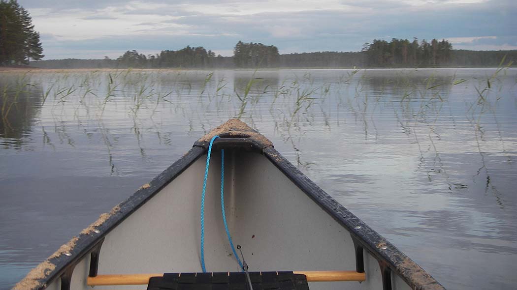 Tyyni järvimaisema, kuvan etualalla on veneen keula.