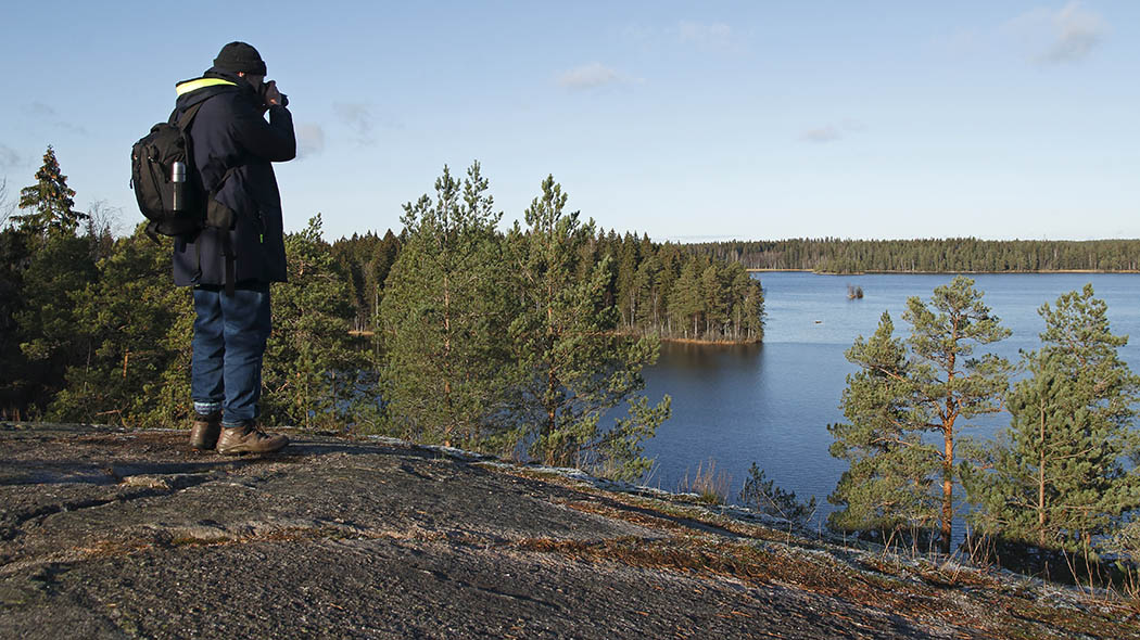 Retkeilijä seisoo kalliolla ja tarkkailee järvelle, joka on metsien ympäröimä.